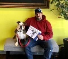Man with bulldog holding Canine Good Citizen certificate indoors
