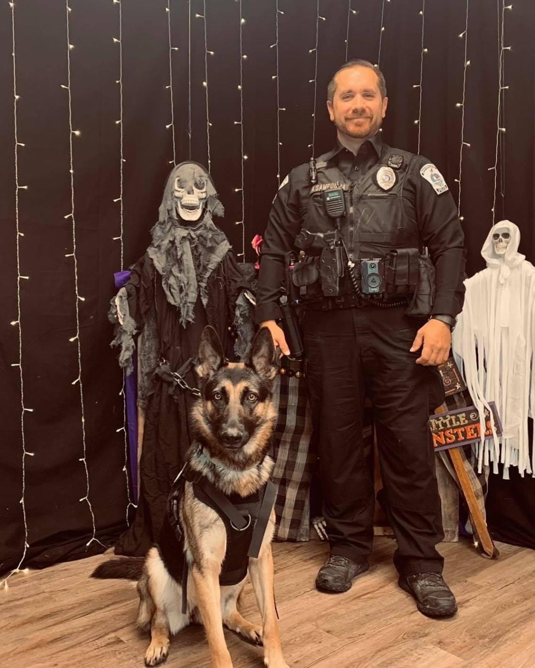 Police officer with K-9 German Shepherd posing at Halloween photo backdrop with skeleton decorations
