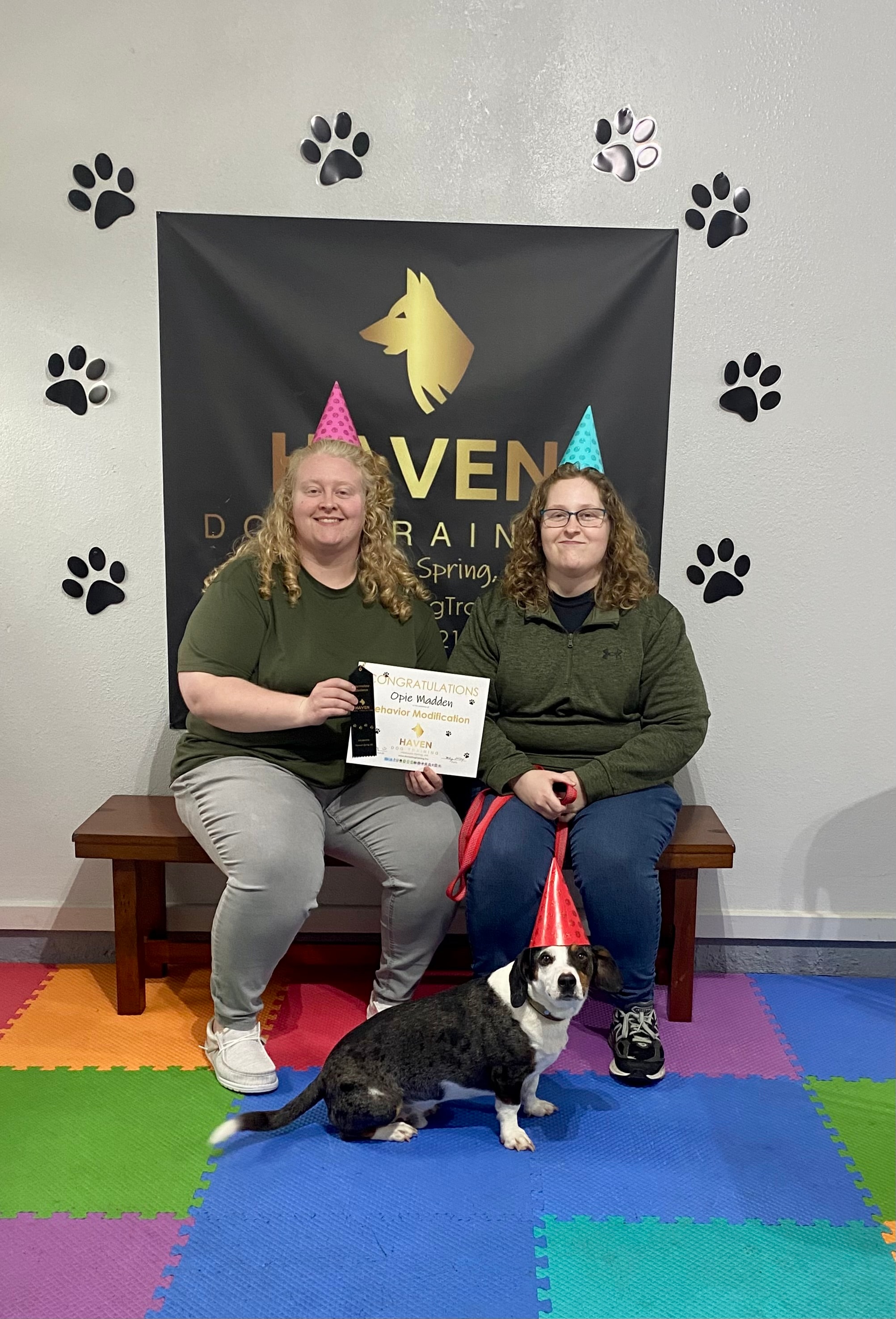 Opie Madden — two women in party hats with Behavior Modification certificate and dog in party hat at Haven banner