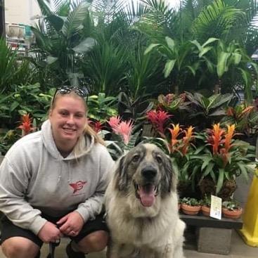 Woman with large fluffy dog posing in front of tropical plants at garden center