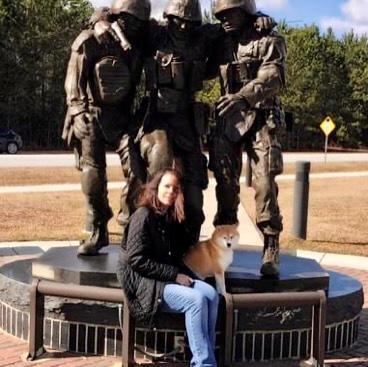 Woman with Shiba Inu therapy dog at military soldiers memorial statue outdoors
