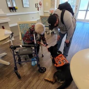Therapy dog Toby in service vest greeting elderly resident with walker