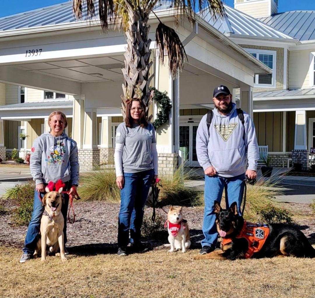 Therapy dog team with three dogs posing outside care facility