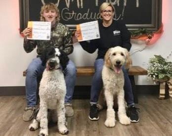 Two women with their certified service dogs holding graduation certificates